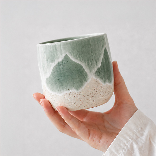 Hand hält eine handbemalten Keramikbecher mit Wellen Design.